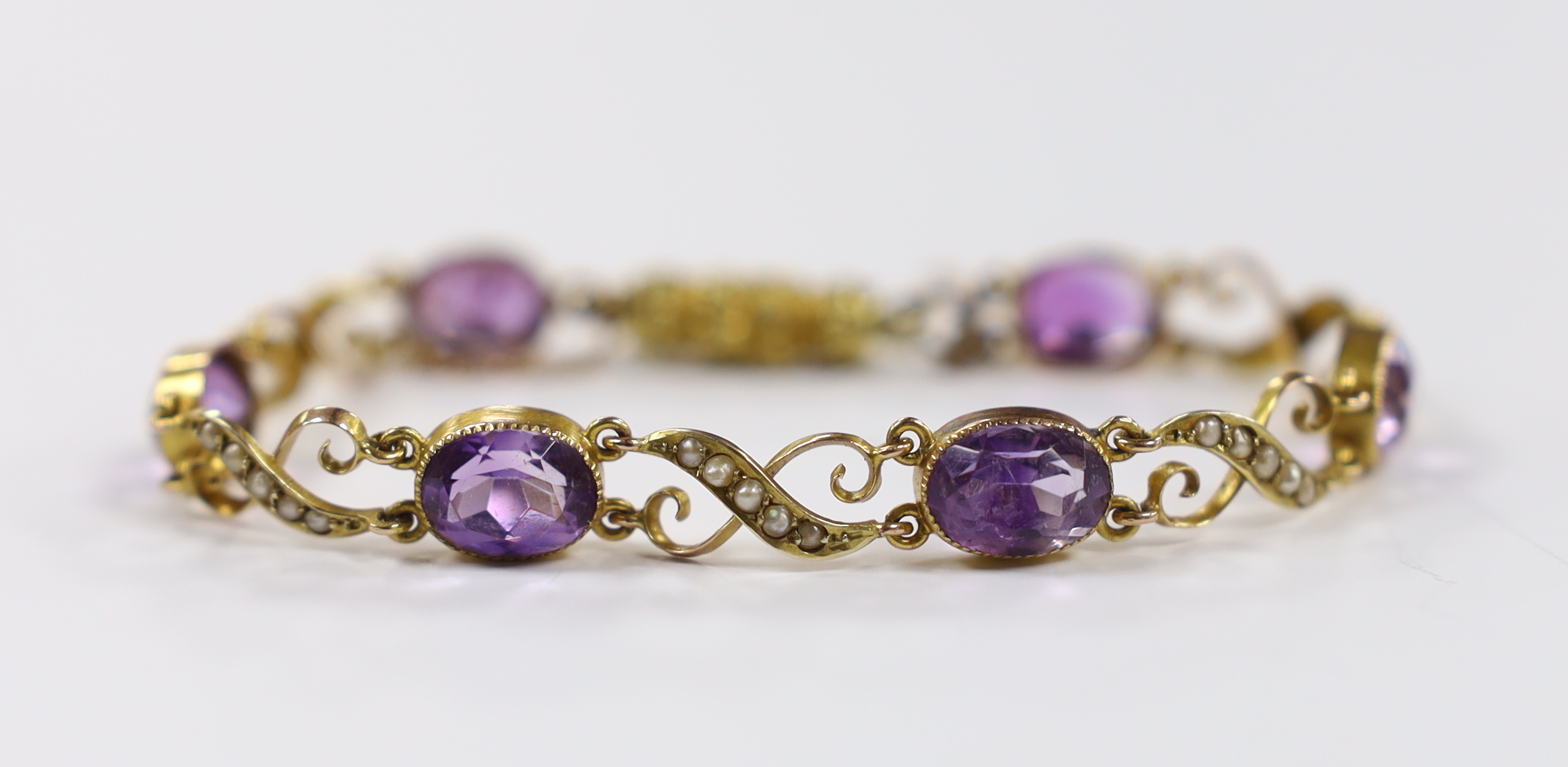 An early 20th century 9ct, amethyst and seed pearl cluster set bracelet, with carved barrel shaped clasp, approx. 16cm gross weight 8.4 grams.